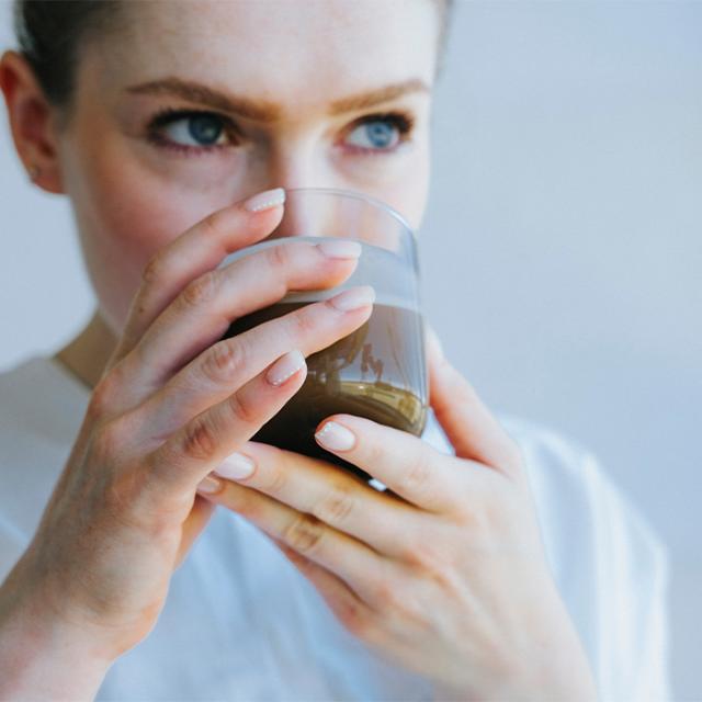 kvinde drikker kaffe fra bryganlæg og industrikaffemaskiner