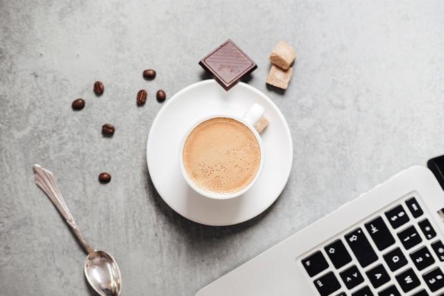 Kaffekop med chokolade ved computer fra kaffemaskine til erhverv